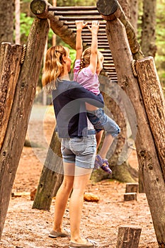 Mother Supporting daughter in the playground with climbing and hanging on a ladder