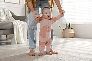 Mother supporting her baby daughter while she learning to walk at home