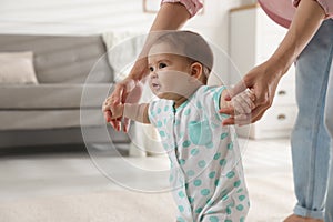 Mother supporting her baby daughter while she learning to walk at home