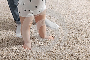 Mother supporting her baby son while he learning to walk on carpet, closeup. Space for text