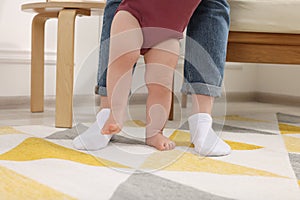 Mother supporting her baby son while he learning to walk on carpet at home, closeup