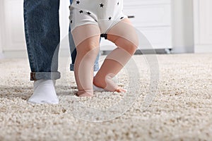 Mother supporting her baby son while he learning to walk on carpet at home, closeup. Space for text