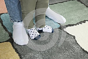 Mother supporting her son while he learning to walk on carpet, closeup. Space for text