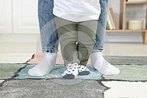 Mother supporting her son while he learning to walk on carpet indoors, closeup