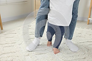 Mother supporting her son while he learning to walk on carpet indoors, closeup. Space for text