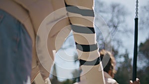 Mother swinging little girl in sunny park close up. African woman pushing swing.