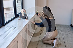 Mother takes photo of infant using smartphone indoors.