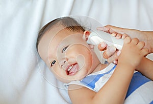 Mother takes temperature for baby boy with ear thermometer on bed at home