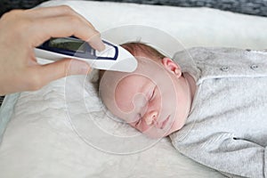 Mother takes temperature for her newborn with infrared thermometer at home