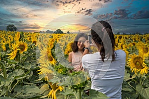 Mother taking photos of daughter in a field surrounded by sunflowers with beautiful sunset