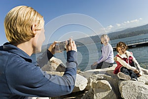 Mother taking picture of daughters at the lake