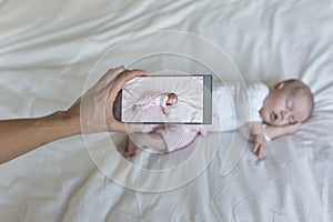 mother taking a picture of her baby girl sleeping on bed. family and love concept