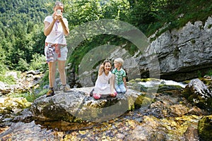 Mother taking a snapshot on a family trip with kids by a mountain stream