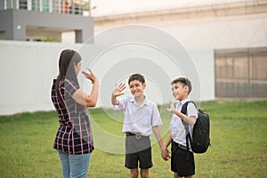 Mother taking sons to school together, hand wave good bye photo