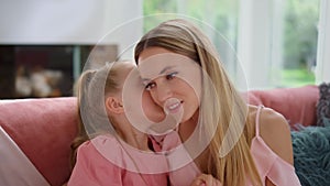 Mother talking with daughter at home. Girl whispering secret on woman ear