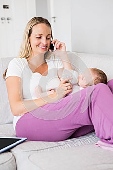 Mother talking on mobile phone while feeding her baby with milk bottle