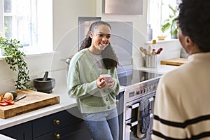 Mother Talking With Teenage Daughter At Home In Kitchen Drinking Hot Drinks Together