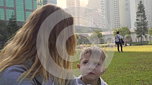 Mother talks to cute little boy on green meadow in city park