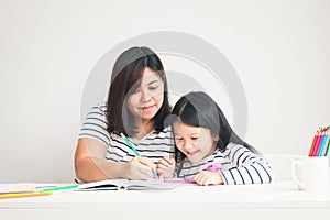 Mother taught homework to the little daughter sitting at the white table in the room. The concept of education for elementary