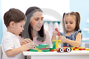 Mother or teacher with children building block toys at home or day care. Kids playing with color blocks. Educational