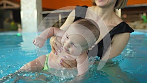 Mother teaches her baby to swim in a closed public pool. The child is swinging on an artificial wave in the aquapark