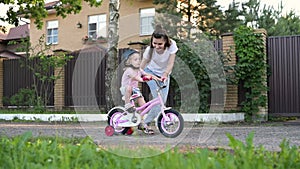 mother teaches her daughter to ride a bike. Little girl in helmet learns to ride