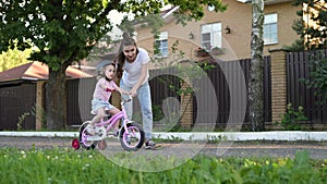 mother teaches her daughter to ride a bike. Little girl in helmet learns to ride