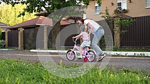 mother teaches her daughter to ride a bike. Little girl in helmet learns to ride