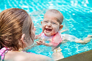 Mother teaches her little baby daughter to swim at the age of 8 months. Summer holiday with infant by the pool at the hotel. Happy