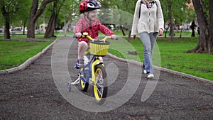 Mother teaches little daughter to ride a bicycle.