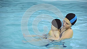 Mother teaches little girl swimming in a pool