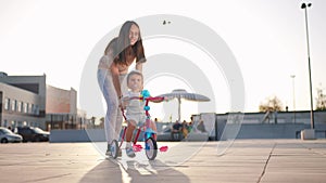 mother teaches son baby to ride a children bike. happy family kid dream concept. child baby rides a bike dad helps