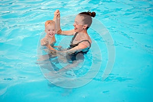 Mother teaches to swim an one-year-old kid in pool