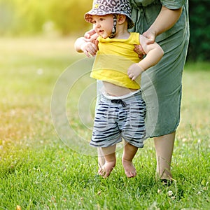 Mother teaches to walk happy toddler baby boy in nature on green gras
