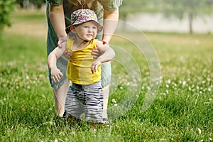 Mother teaches to walk happy toddler baby boy in nature on green gras