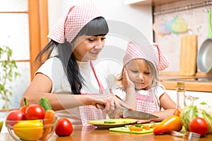 Mother teaching child making salad in kitchen. Mom and kid chopping vegetable on cutting board with knife. Cooking concept of