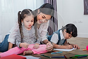 Mother teaching children in drawing class. Daughter and son painting with colorful crayon color in home. Teacher training students