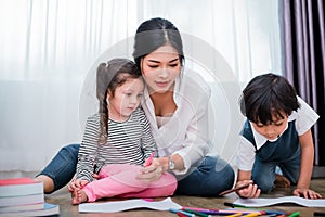 Mother teaching children in drawing class. Daughter and son painting with colorful crayon color in home. Teacher training students