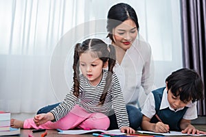 Mother teaching children in drawing class. Daughter and son painting with colorful crayon color in home. Teacher training students