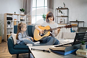 Mother teaching cute little musician girl to play guitar.