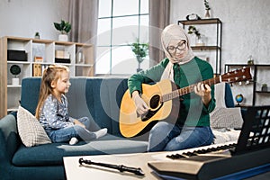 Mother teaching cute little musician girl to play guitar.