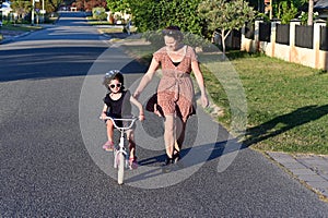 Mother teaching daughter to ride bike in city street front view