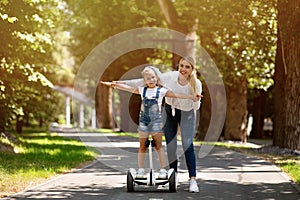 Mother Teaching Daughter To Ride A Segway In City Park