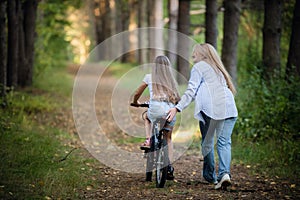 Mother teaching her daughter cycling in a forest outdoors