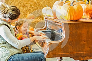 Mother teaching her daughter how to play piano in halloween season - Mom and little girl enjoying pumpkin patch