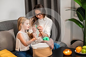 Mother teaching her daughter to knot on sofa in home interior knitting with her daughter