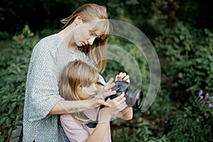 Mother is teaching her young daughter to use a camera outside in spring nature