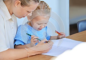 Mother teaching little daughter during homeschool class at home. Cute little caucasian girl learning how to read and