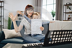 Mother teaching playing piano using notes her daughter.