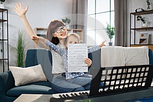 Mother teaching playing piano using notes her daughter.